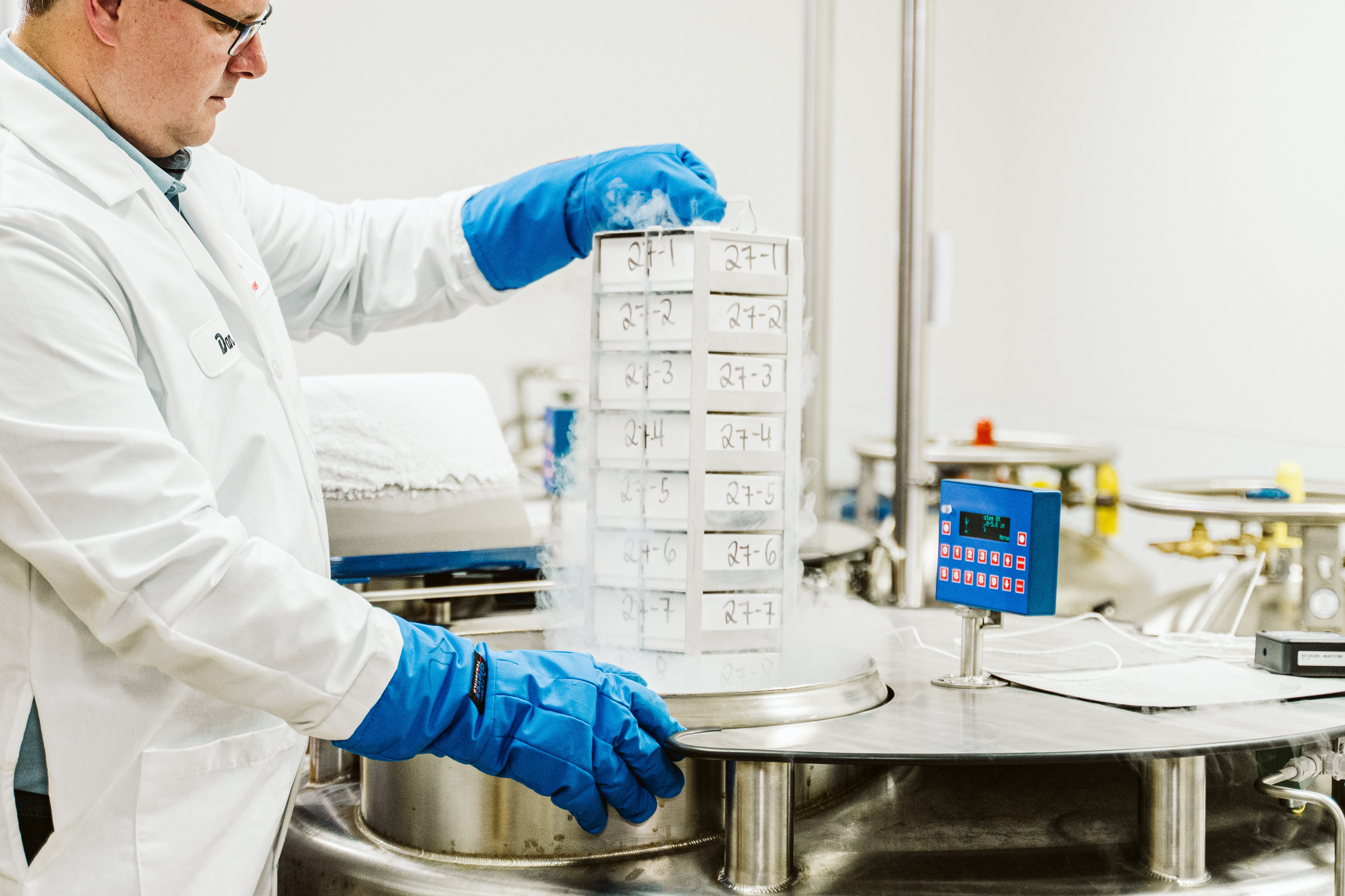 A scientist handles a rack of biological samples over a barrel used for cold storage.